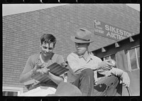 Fruit auctioneer and clerk eating peaches in front of livestock pavilion, Sikeston, Missouri by Russell Lee