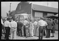 Groups of people standing in front of weighing concession with owner trying to drum up trade, state fair, Donaldsonville, Louisiana by Russell Lee
