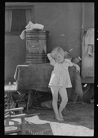 Child of migrant family in front of household goods of trailer home, Weslaco, Texas by Russell Lee