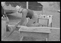 White migrant worker sawing wood for stakes to be used in setting up tent home, near Harlingen, Texas by Russell Lee