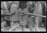 Oil field workers releasing pipe wrenches from drill pipe, oil well, Kilgore, Texas by Russell Lee