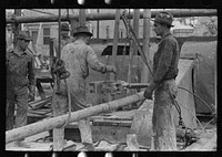 [Untitled photo, possibly related to: Oil field workers releasing pipe wrenches from drill pipe, oil well, Kilgore, Texas] by Russell Lee