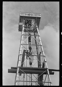 Top of derrick showing gin pole, crow's nest, crown block, traveling block, elevator and cat line. Oil well, Kilgore, Texas by Russell Lee