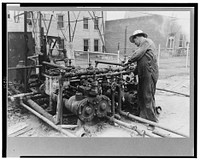 Oil field worker working on the mud hog, a machine which pumps the mud from the sluch pit through the drill pipe to the bit, Kilgore, Texas by Russell Lee