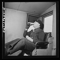 Rear brakeman George Clark having his lunch in the cupola of the caboose on the Atchison, Topeka, and Santa Fe Railroad, between Marceline, Missouri and Argentine, Kansas. The bottle contains hot coffee. Sourced from the Library of Congress.