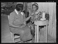 [Untitled photo, possibly related to: Nurse Shamburg gives Viola Pettway instructions and help about her diet in treatment of pellagra. She has been sick about four years and is a little better now. Her mother has thirteen children and twenty-five dollars a month for all. Table top is made from cheese box. Gee's Bend, Alabama]. Sourced from the Library of Congress.