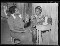 Nurse Shamburg gives Viola Pettway instructions and help about her diet in treatment of pellagra. She has been sick about four years and is a little better now. Her mother has thirteen children and twenty-five dollars a month for all. Table top is made from cheese box. Gee's Bend, Alabama. Sourced from the Library of Congress.
