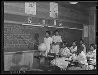 English lesson in sixth and seventh grade school room. Selma Sutton at board with teacher, Miss Jessie West Greene. Flint River Farms, Georgia. Sourced from the Library of Congress.