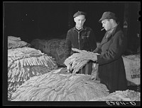 Tobacco warehouseman examining farmer's tobacco before auction sale. Durham, North Carolina. Sourced from the Library of Congress.