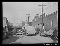 Street showing several tobacco warehouses on day of auction sales with farmers bringing in their tobacco on trailers and trucks. Mebane, Orange County, North Carolina. Sourced from the Library of Congress.