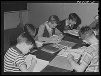 Children of workmen at the Umatilla ordnance depot attend school in basement of church, use long tables as desk. Hermiston, Oregon by Russell Lee