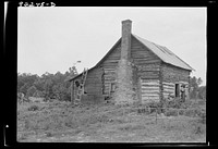 [Untitled photo, possibly related to:  sharecropper house. Note chimney leanto with kitchen stove pipe stuffed through side of wall and cap off with joint of tobacco flue to keep smoke from blowing back into house. Note also flower garden protected by slender fence of lathes. Person County, North Carolina]. Sourced from the Library of Congress.