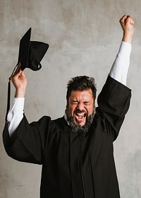 Cheerful man in a graduation gown holding his mortarboard 