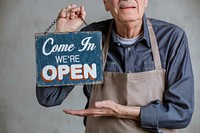 Senior man holding shop sign plate, come in we 're open