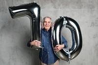 Cheerful senior man holding silver balloons for his 70th birthday celebration