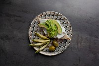 Healthy avocado toast serves on a modern patterned plate with olives flatlay