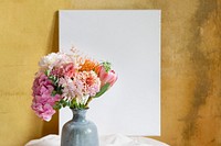 Blank board against a yellow wall by a vase of flowers