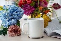 White coffee cup mockup among flowers on a table