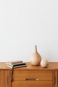 Stack of notebooks by a wooden vase on a wooden cabinet in a white room