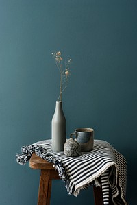 Gray ceramic vase with a mug on a wooden stool by a forest green wall 