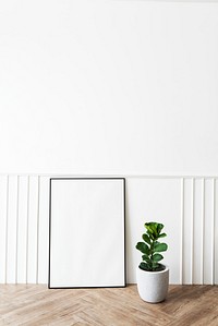Blank picture frame by a fiddle-leaf fig plant on a parquet floor
