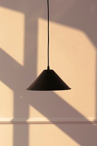 Black pendant lamp with a late afternoon light on a beige wall