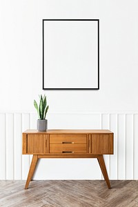Picture frame over a wooden sideboard table with a snake plant in a vase
