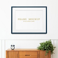 Black picture frame mockup hanging over the wooden cabinet