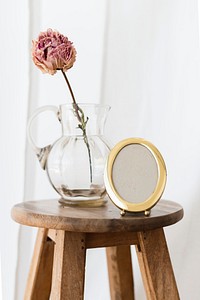 Dry peony flower in a glass jug on a wooden stool in a white room