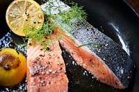 Grilled salmon fillet being sprinkled with salt and pepper