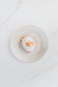Donut decorated with sprinkles served on a white marble table