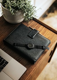 Black planner on a wooden desk by a laptop