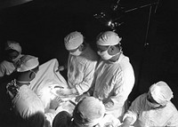 The 1950s historical photograph of the inside of an operating room suite during a surgical procedure.