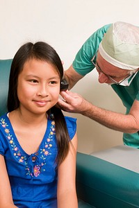 A clinician conducting an examination of a young female patient&rsquo;s left ear, using an otoscope.