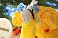 Healthcare worker donning the final article of personal protective equipment (PPE), a plastic apron, which would complete his protective uniform.