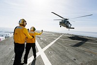 On the top deck of the USS San Diego, U.S. Navy personnel monitor a helicopter landing. Original from NASA. Digitally enhanced by rawpixel.