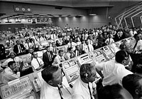 Members of the Kennedy Space Center government-industry team rise from their consoles within the Launch Control Center to watch the Apollo 11 liftoff through a window.