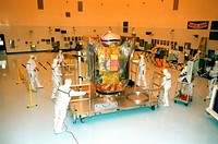 In the Payload Hazardous Service Facility, workers move the Stardust spacecraft on its workstand from the air lock to the high bay. Original from NASA. Digitally enhanced by rawpixel.