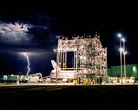 Lightning strikes in the distance as the Space Shuttle Discovery receives post-flight processing in the Mate-Demate Device. Original from NASA. Digitally enhanced by rawpixel.