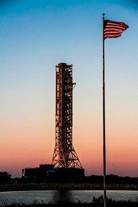 The flag at NASA&#39;s Press Site is on guard as the mobile launcher, or ML, passes by the turn basin at NASA&#39;s Kennedy Space Center in Florida. Original from NASA . Digitally enhanced by rawpixel.