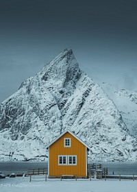 Yellow cabin framed by the snowy peak on Lofoten islands, Norway