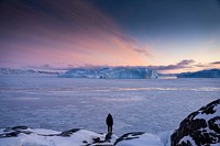 Man watching the sun setting over the frozen sea in Greenland