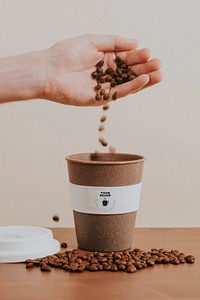 Hand pouring coffee beans into a cork coffee cup