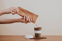 Hand pouring coffee beans from a paper bag into a coffee cup