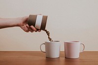 Hand pouring coffee beans into a ceramic mug