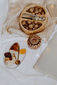 Walnuts in a wooden box, a laptop, and a plate of croissant on a white bed