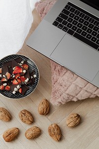 Dark chocolate brittle and walnuts on a wooden floor next to a laptop