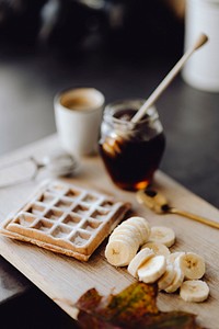 Waffle and slices of banana on a wooden tray next to a honey jar