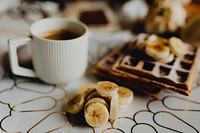 Plate of waffle with slices of banana and a cup of coffee