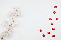 Valentine&#39;s white orchids with red chocolate hearts on a white marble background